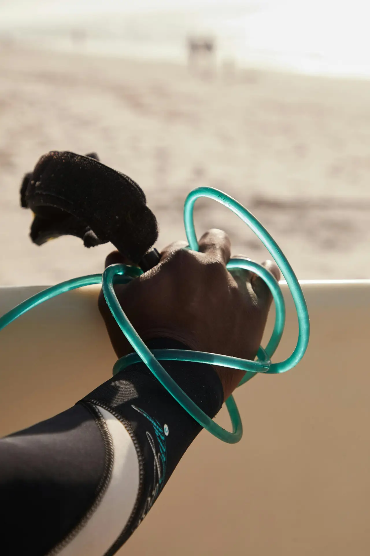 Close-up of a surfer's hand holding a surfboard leash on a sunny beach, ready for action.